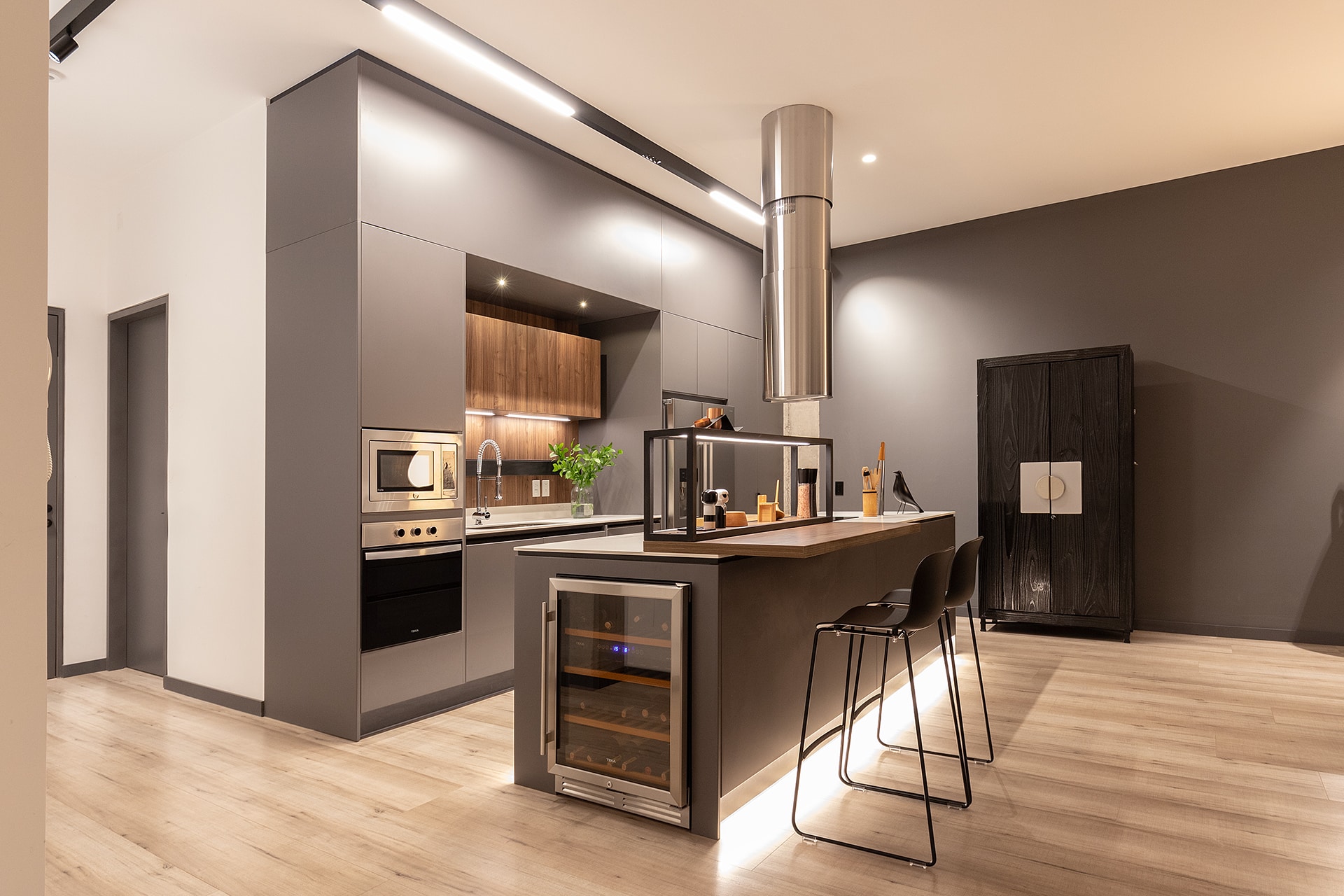 Modern kitchen with gray cabinets, an island, bar stools, wood accents, and stainless steel appliances.