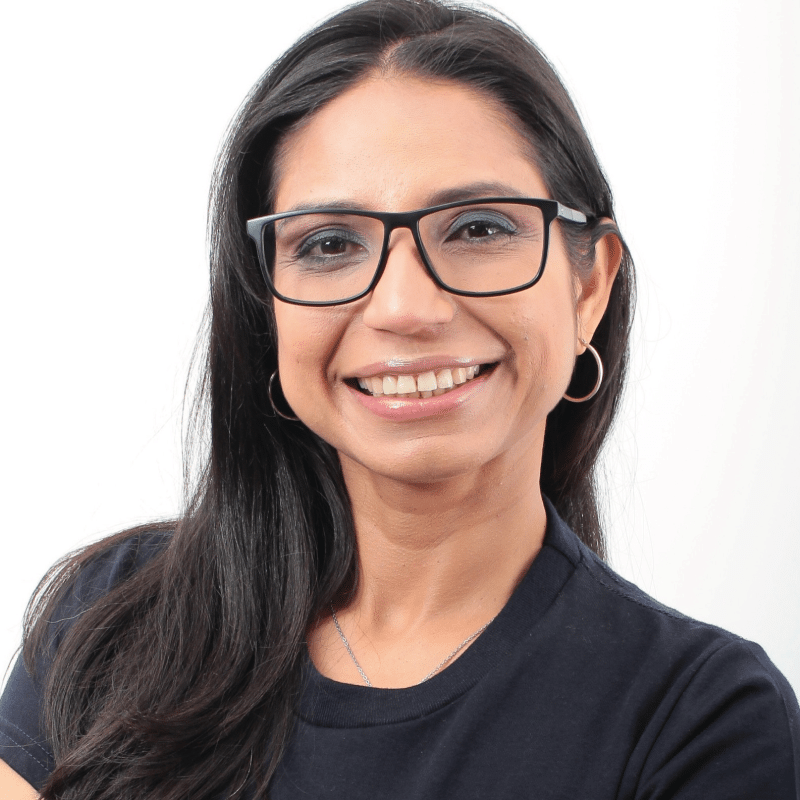 Smiling woman with glasses, dark hair, wearing a navy shirt, against a white background.
