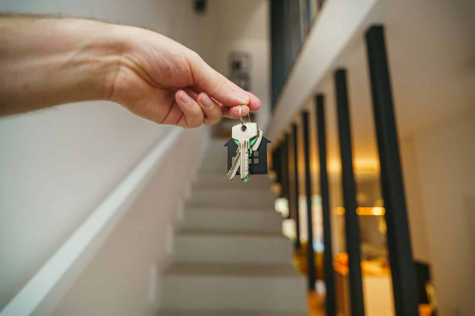 Hand holding house keys with a staircase in the background.