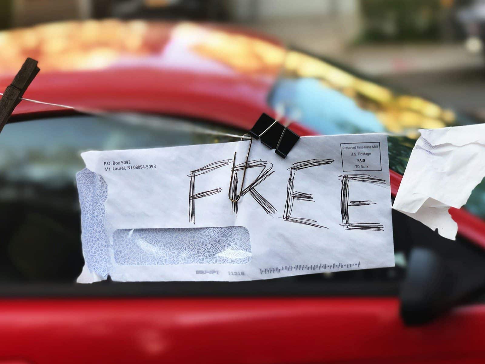 Envelope with "FREE" written on it, clipped to a red car window.