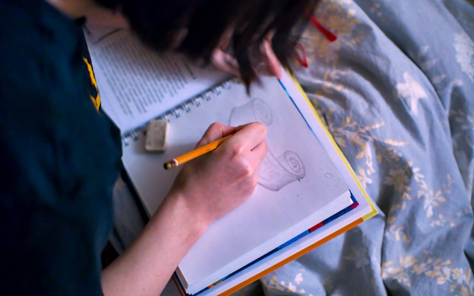 Person sketching a spiral design in a notebook with a pencil, eraser nearby.